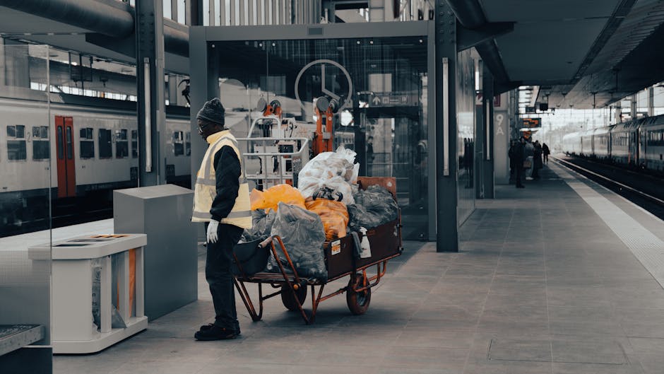 A person wearing dark clothing, gloves, and a beanie hat stands next to a large metal trolley loaded with various bags of waste, including black, grey, and orange plastic sacks, some of which are part